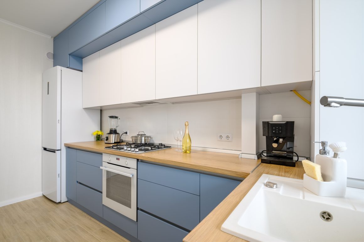 Cuisine avec façades bleues et blanches, plan de travail en bois, électroménagers posés et évier