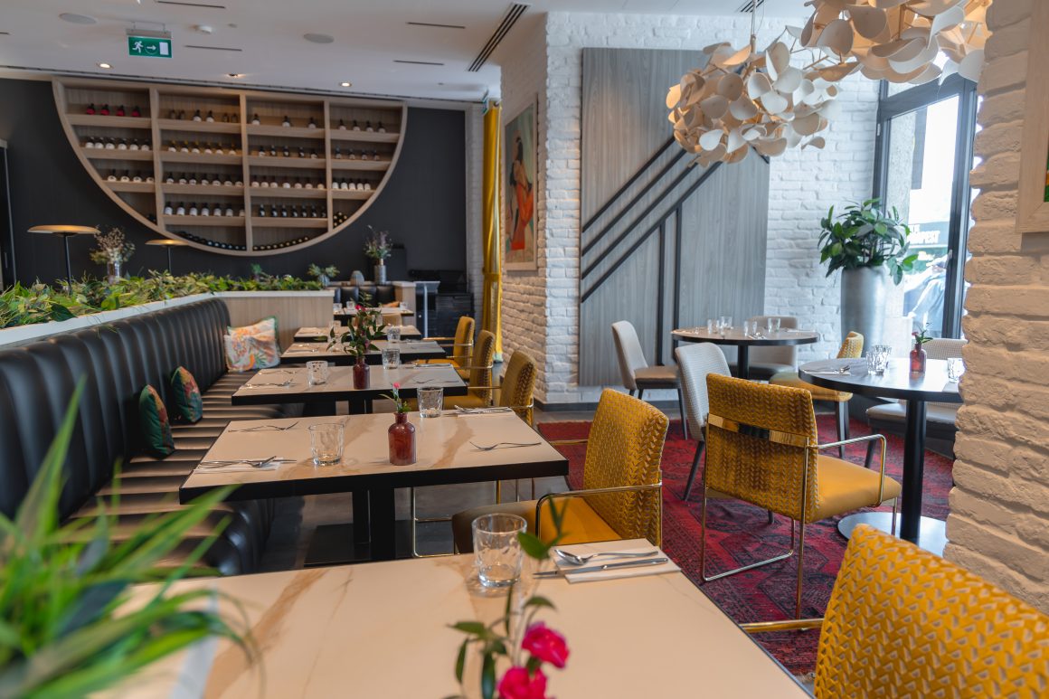 Restaurant chaleureux avec tables, sièges jaunes, banquette cuir, plantes et lumière douce