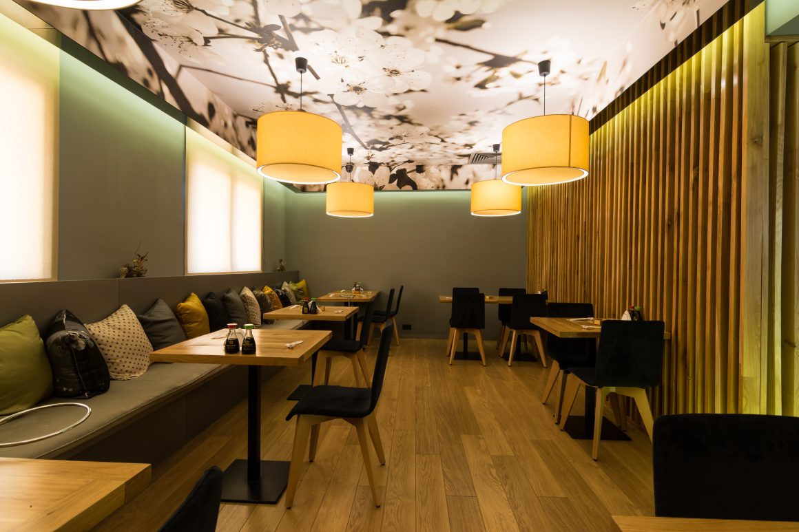Conception restaurant incluant mur en lattes, banquettes, tables en bois, chaises noires et luminaires