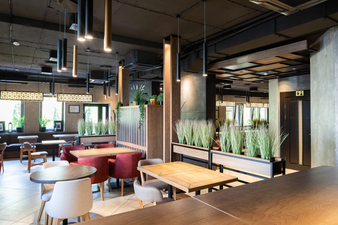 Aménagement restaurant avec tables en bois, plantes, banquettes et luminaires suspendus