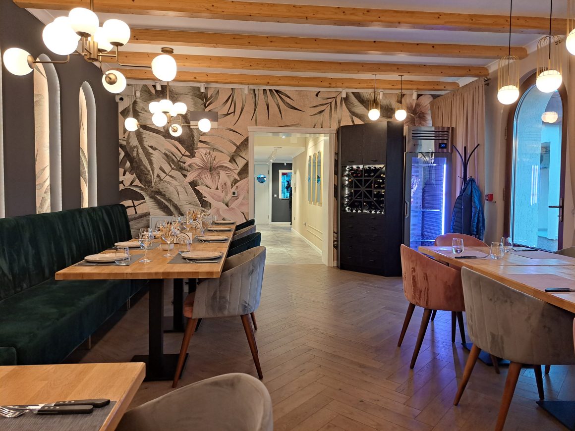 Restaurant inclut tables en bois, banquette verte, chaises pastel, décor tropical et éclairage suspendu