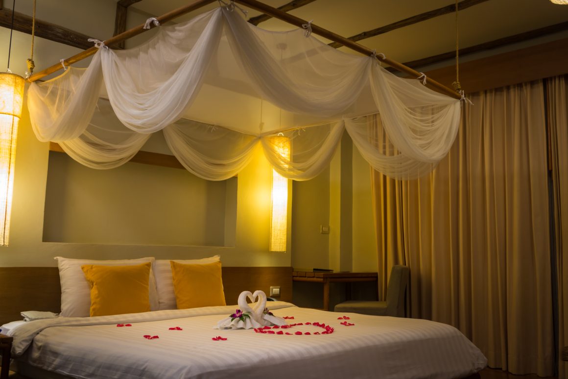 Déco chambre Saint Valentin : lit à baldaquin avec pétales de rose en cœur et éclairage doux