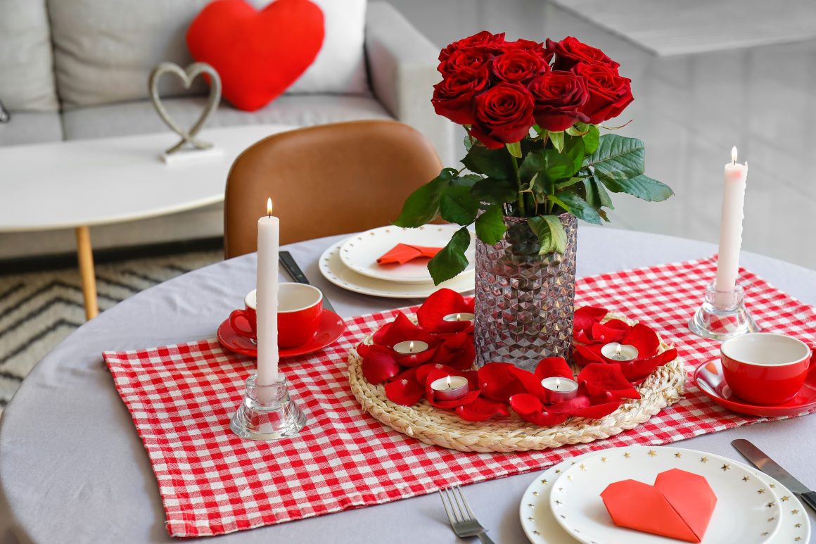 Table romantique décorée de roses rouges, pétales, bougies et serviettes en forme de cœur
