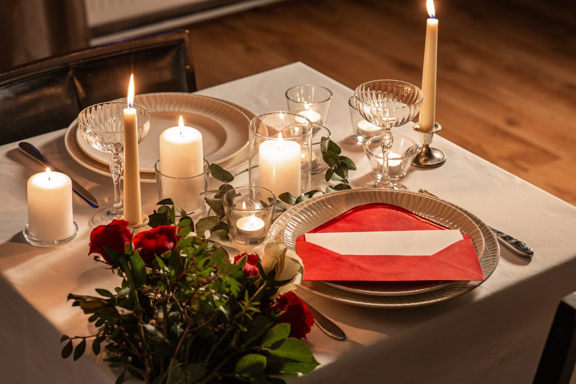 Table dressée romantique : bougies allumées, roses rouges, vaisselle élégante et enveloppe rouge
