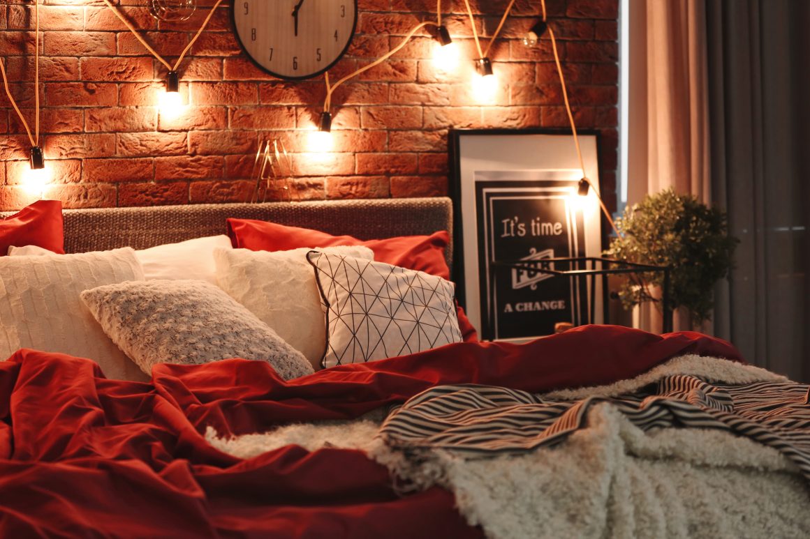Chambre chaleureuse avec briques apparentes, éclairage tamisé, literie rouge et coussins moelleux