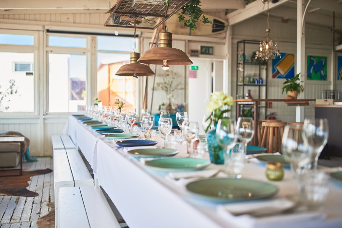 Table élégante dressée avec vaisselle colorée, verres étincelants, décor floral et suspensions en cuivre.