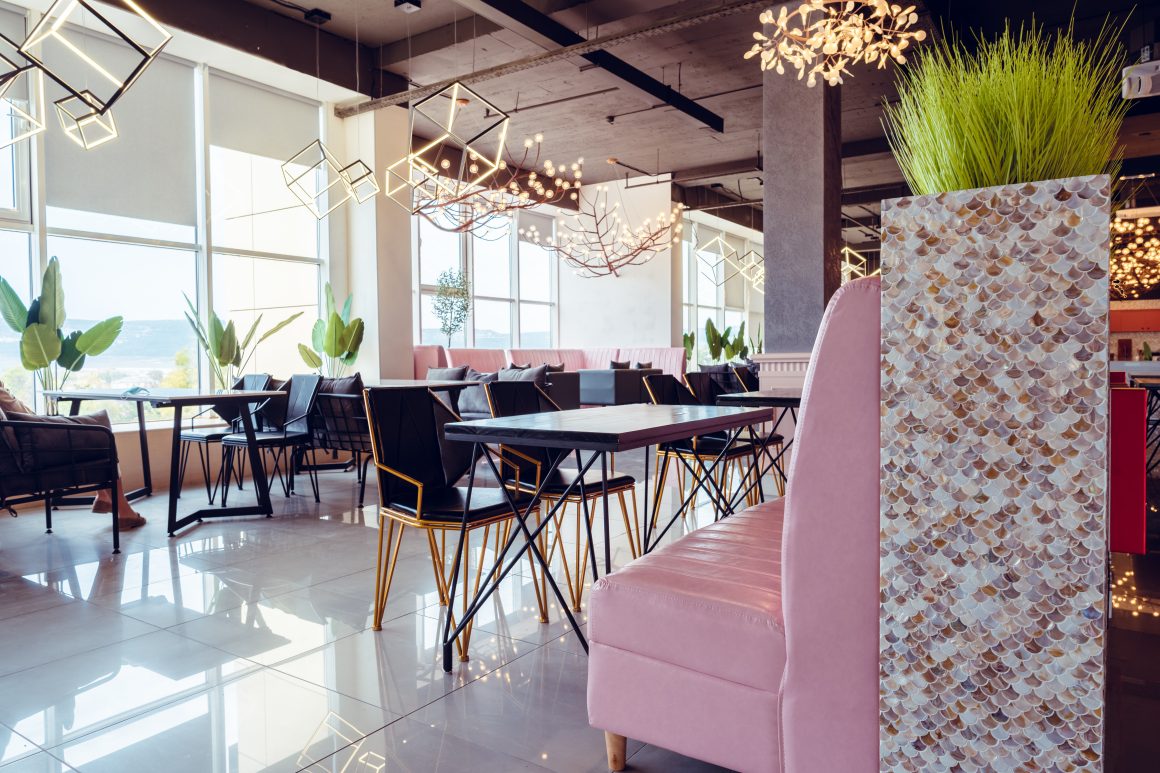 Aménagement intérieur restaurant avec banquettes roses, chaises noires, plantes et suspensions géométrique
