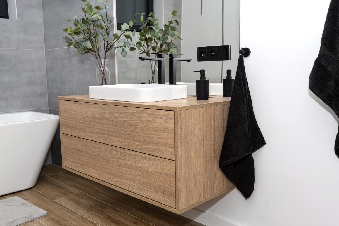 Meuble lavabo flottant en bois, incluant vasque blanche, robinet noir, plantes et serviettes noires