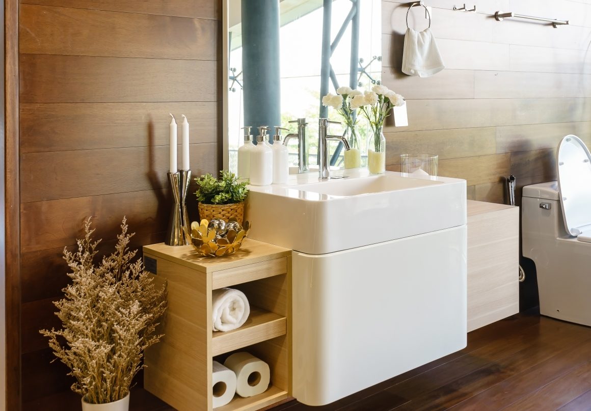 Salle de bain en bois incluant lavabo blanc, étagères avec serviettes, plantes et bougies décoratives