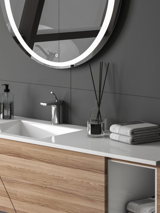 Tendance meuble salle de bain avec vasque blanche, miroir rond éclairé, serviettes et accessoires gris et noir
