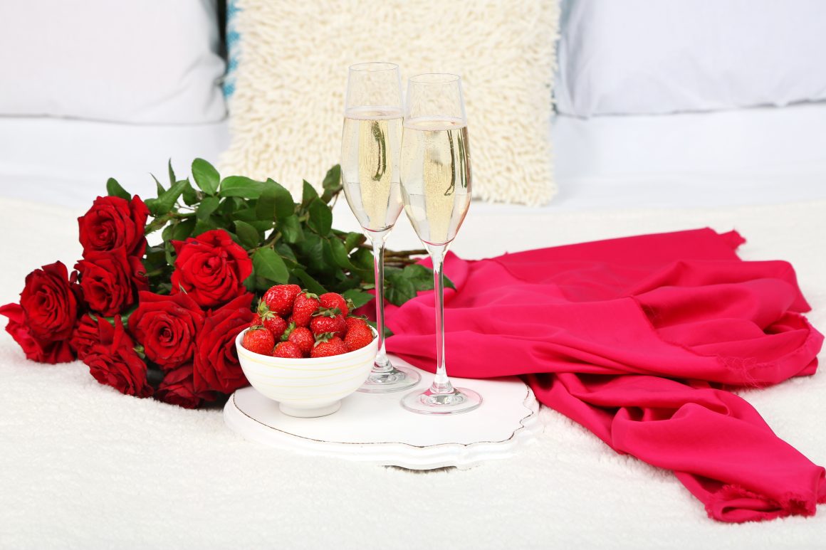Lit avec des fleurs rouges et un plateau incluant fraises et champagne