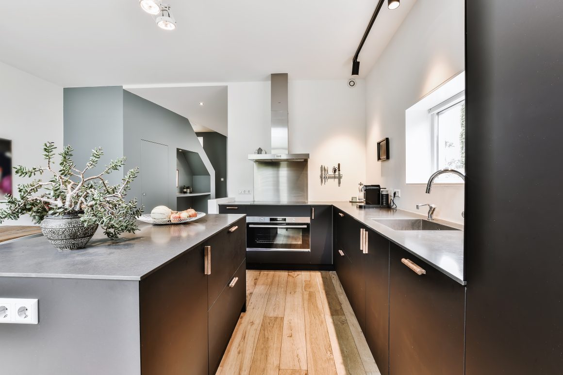 Cuisine épurée avec îlot, meubles gris foncé, plan de travail gris, électroménagers inox et sol en bois clair