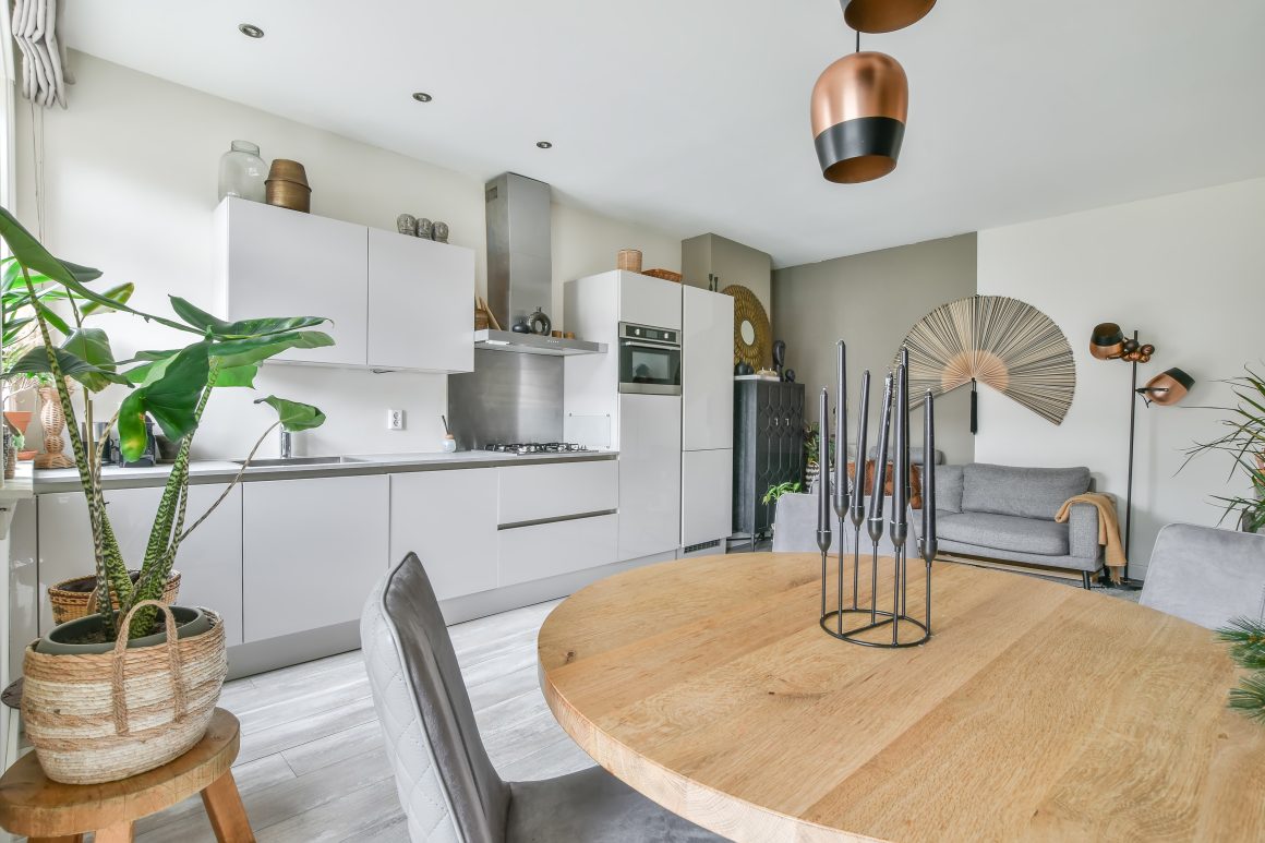 Cuisine ouverte avec meubles blancs, plan de travail gris, électroménagers, table ronde bois et plantes