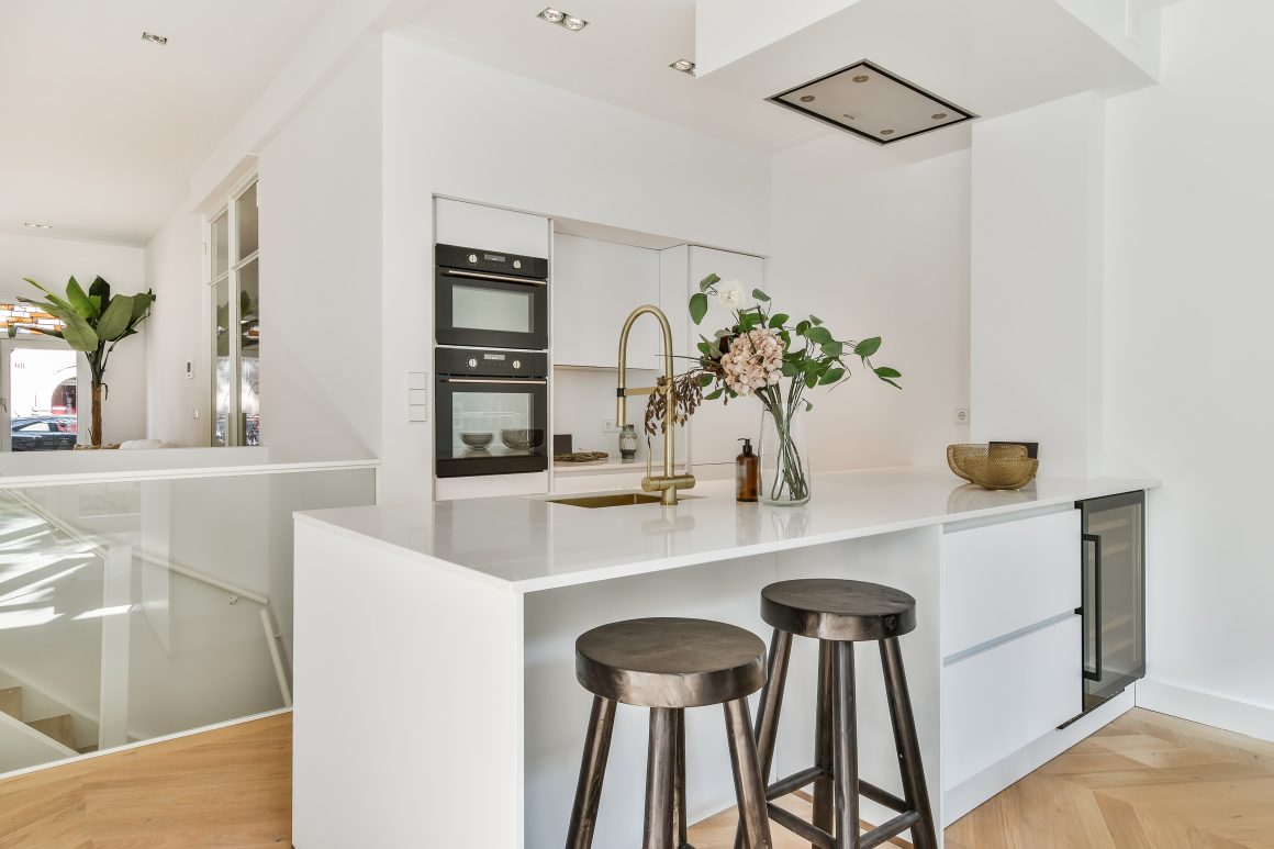 Cuisine incluant électroménager encastré et un îlot central blanc avec robinet doré et tabourets en bois