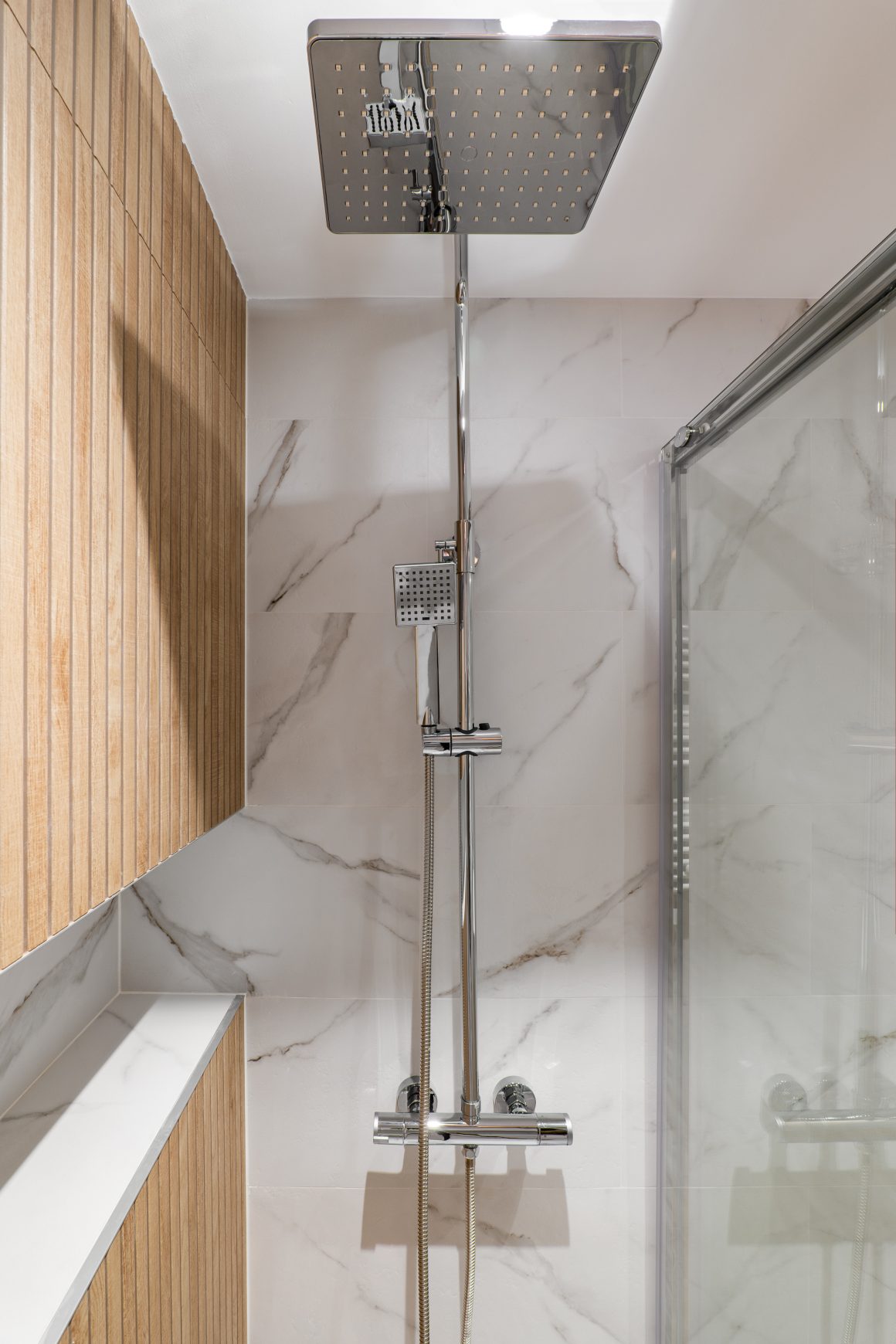 Douche moderne avec pommeau carré, robinetterie chromée, carrelage marbré et paroi vitré