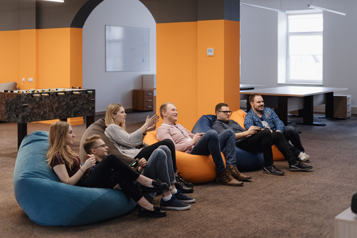 Groupe détendu sur poufs dans une salle de repos moderne aux tons orange et gris avec baby-foot