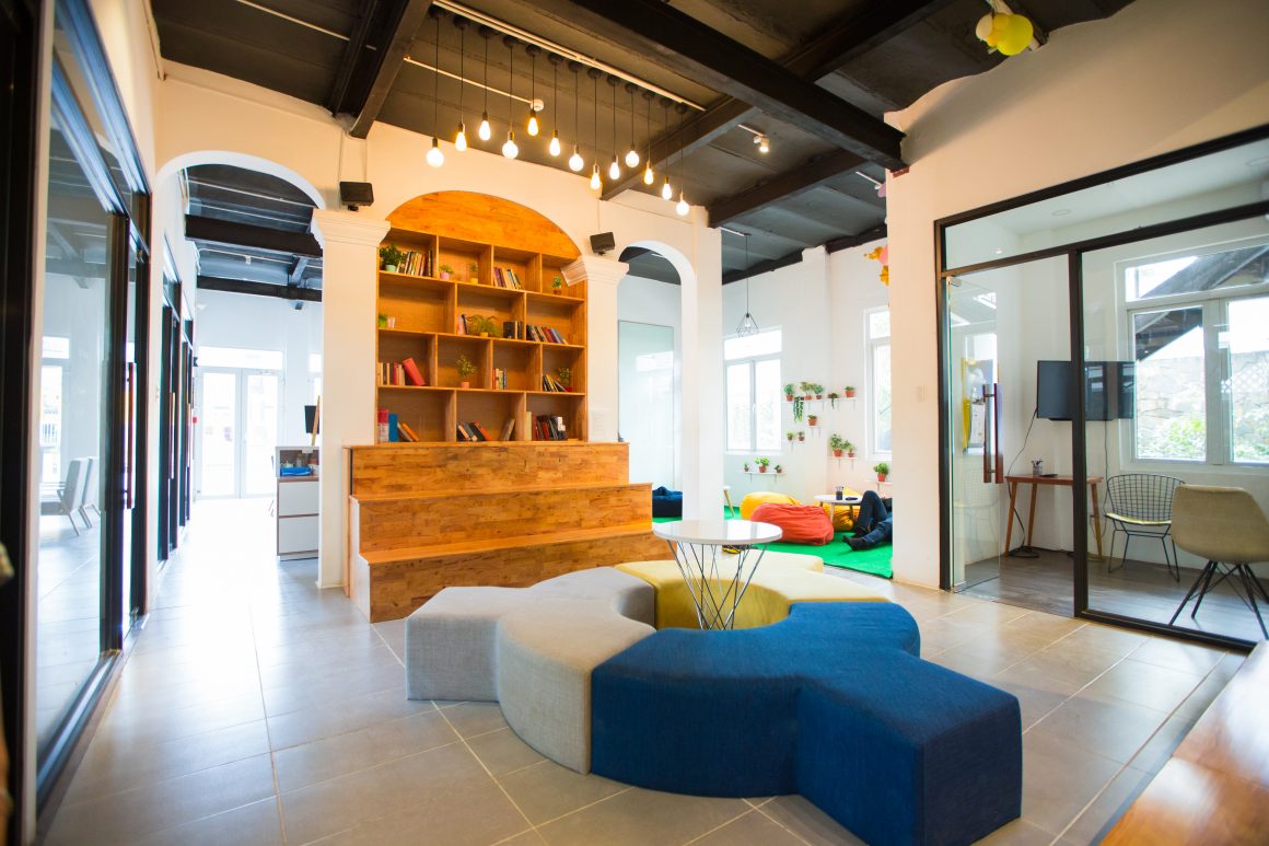 Aménagement salle de repos entreprise avec poufs, tables basses, sièges modulaires et étagères en bois