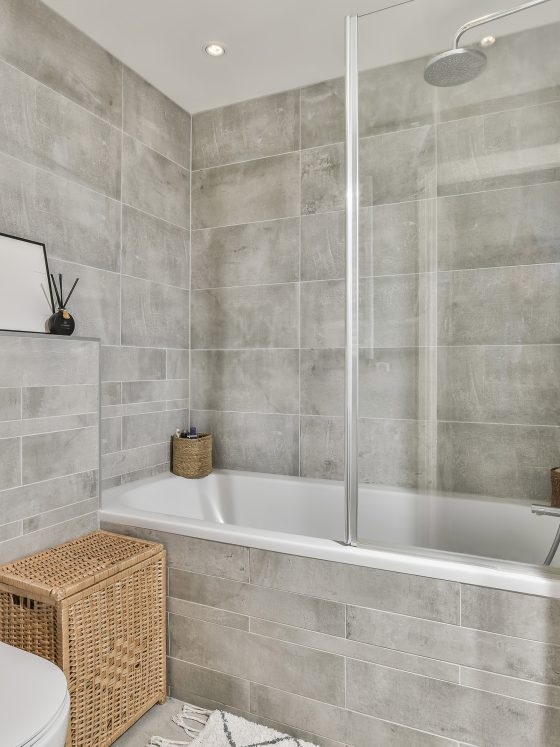 Baignoire vitrée avec carrelage de salle de bain gris texturé, couvrant murs et sol, et accessoires naturels