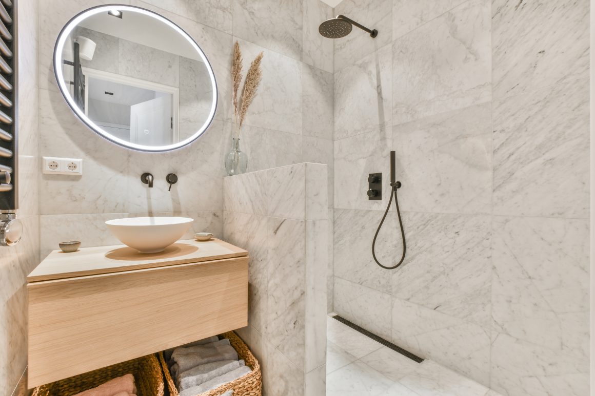 Salle de bain en marbre blanc incluant miroir éclairé, meuble en bois et douche