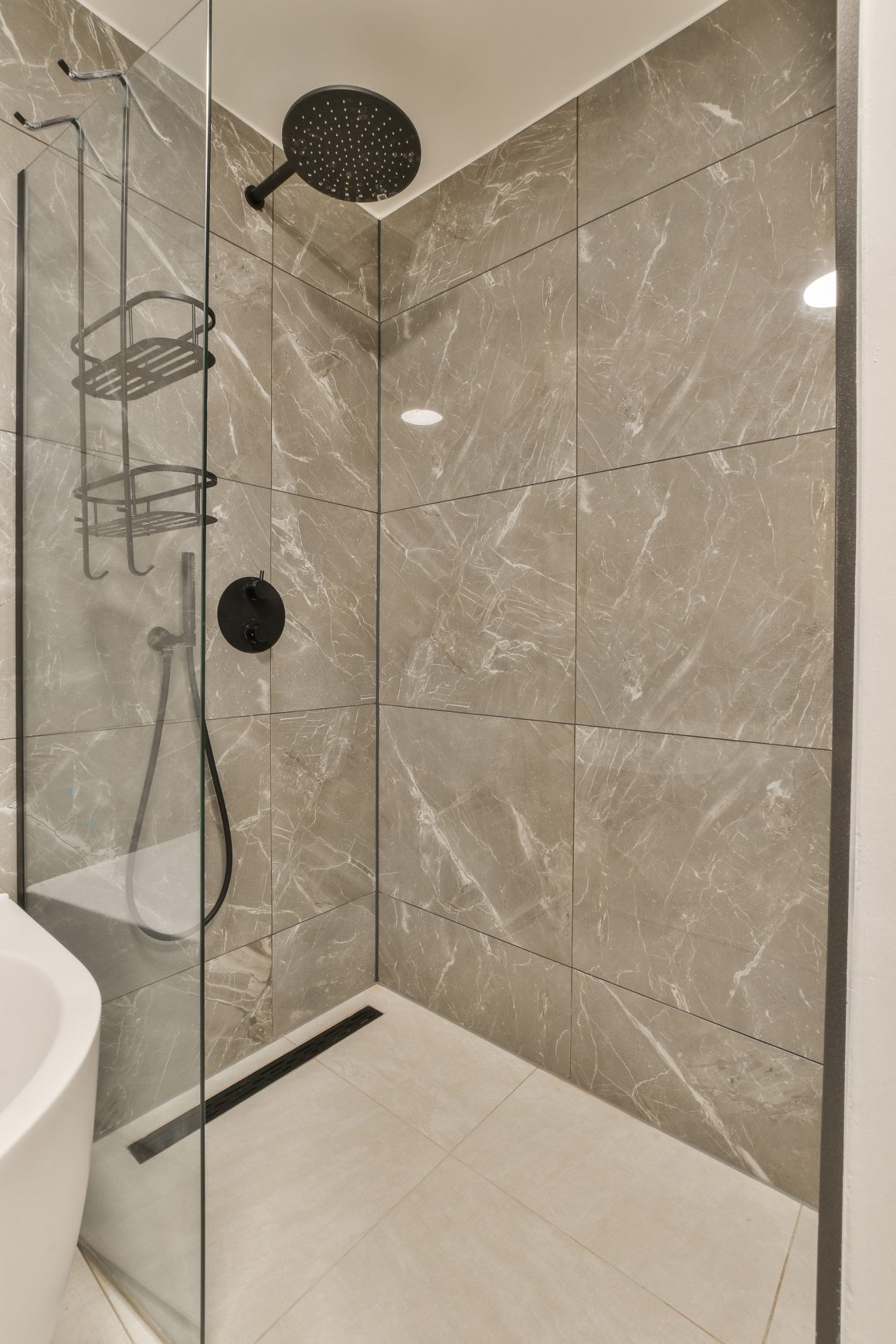 Douche vitrée avec carrelage gris brillant, pommeau noir et mitigeur mural
