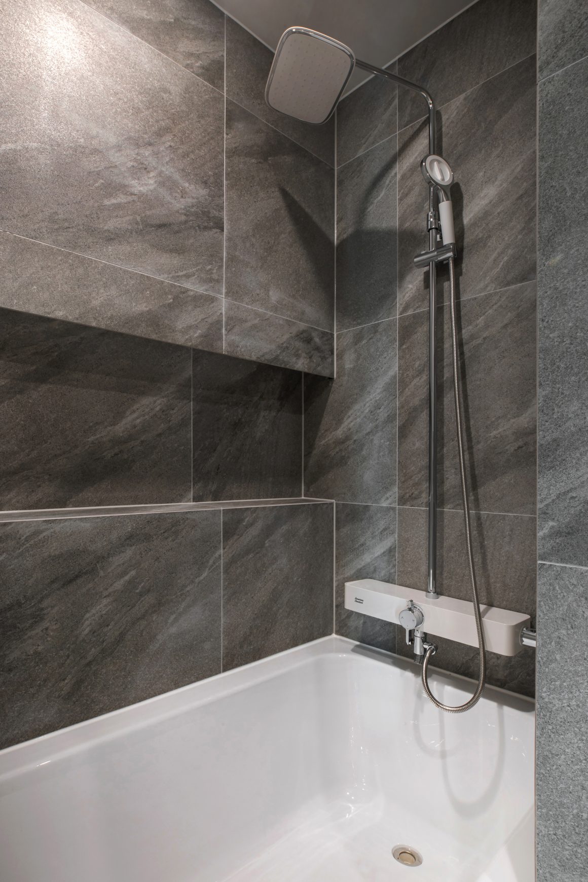 Salle de bain incluant baignoire blanche avec carrelage gris marbré et douchette