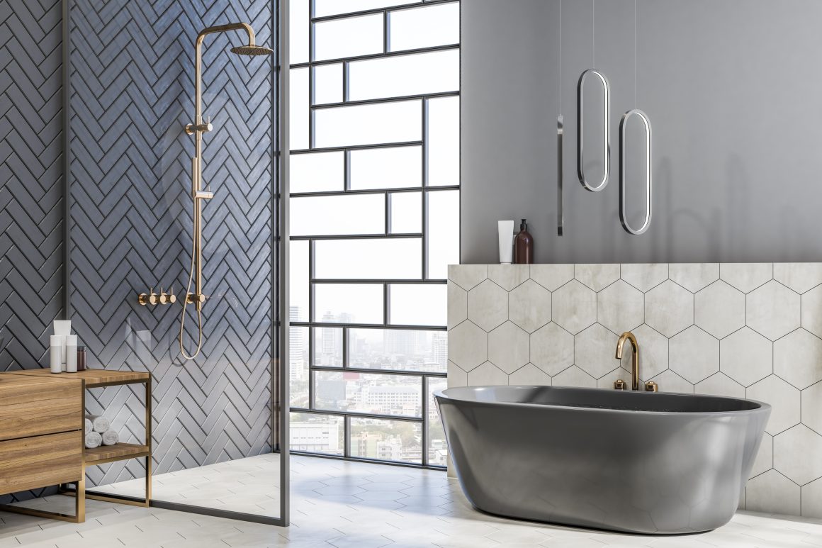 Baignoire îlot en gris foncé avec robinet doré, carrelage hexagonal, douche vitrée à chevrons et meuble en bois