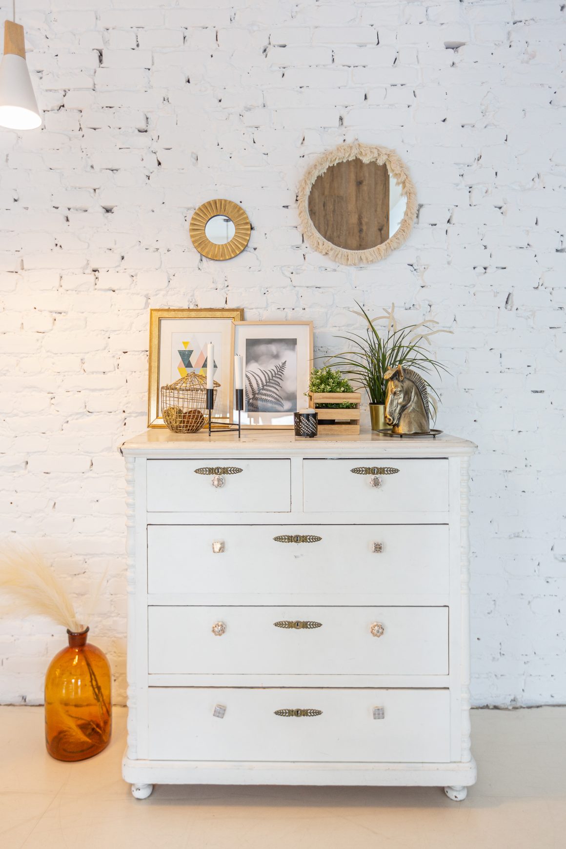 Déco commode chambre bohème avec miroirs ronds, cadres, plante, bougies et buste de cheval