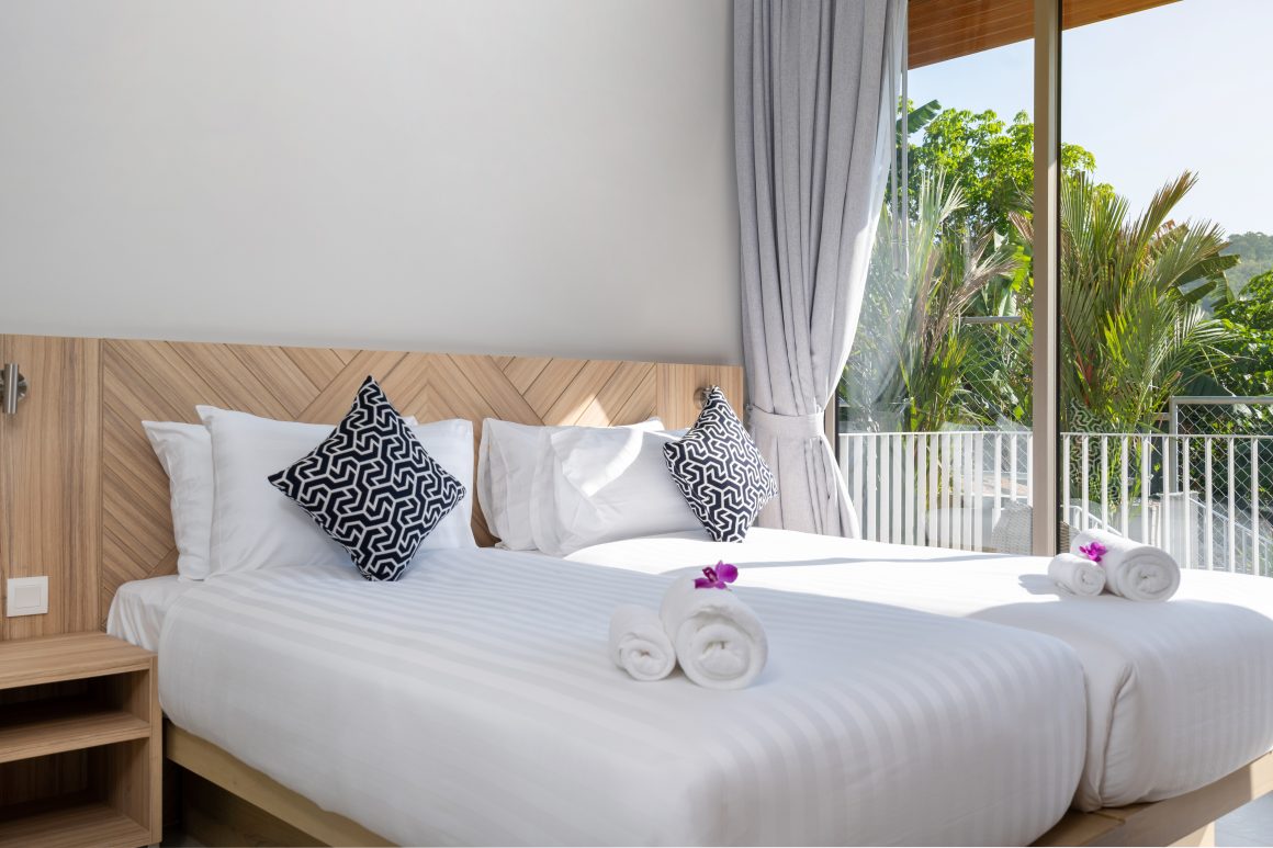 Chambre lumineuse incluant deux lits avec linge blanc, et serviettes roulées avec orchidées