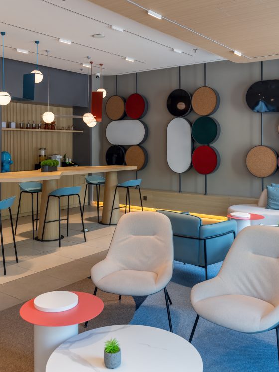 Aménagement salle de pause entreprise avec bar en bois, tabourets, canapé, fauteuils et décor mural circulaire