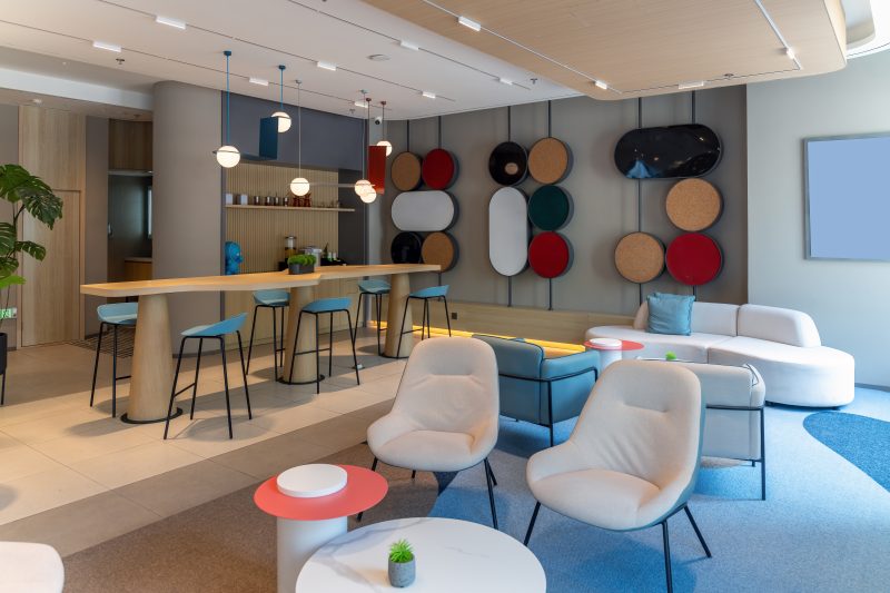 Aménagement salle de pause entreprise avec bar en bois, tabourets, canapé, fauteuils et décor mural circulaire