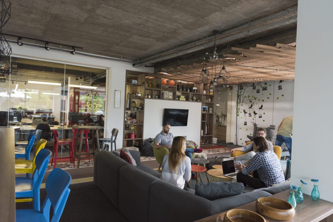 Open-space lumineux incluant canapé gris, sièges colorés et tables en bois