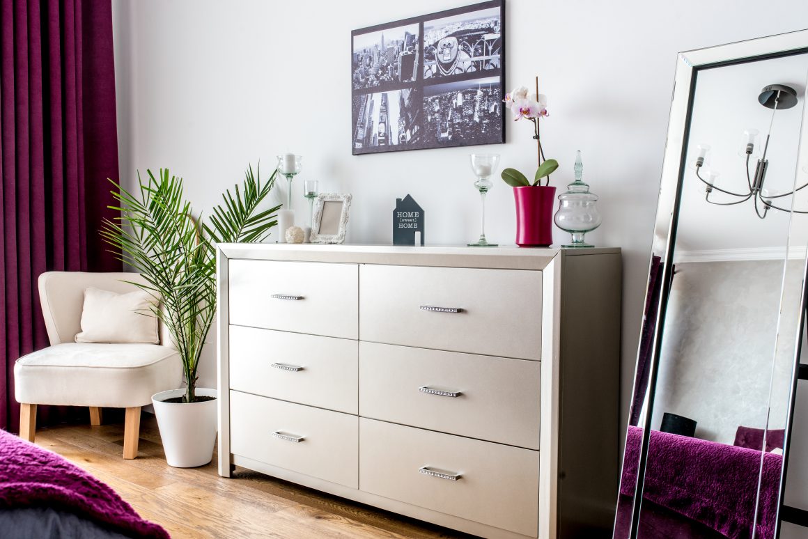 Commode beige claire à six tiroirs avec poignées métalliques, décorée d'objets et d'une orchidée