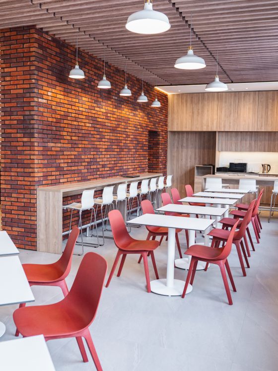 Aménagement réfectoire entreprise avec tables, chaises, comptoir à tabourets, mur en brique et cuisine