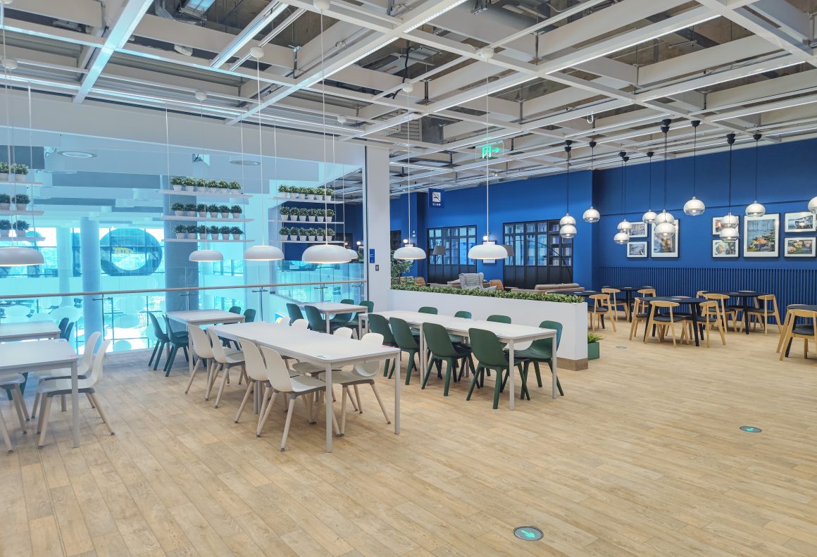 Aménagement réfectoire entreprise avec parquet clair, tables, chaises, suspensions et plantes