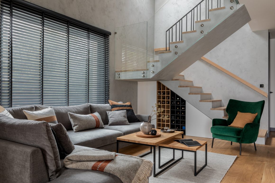 Salon moderne sous escalier aménagé avec canapé gris, fauteuil vert, table en bois et tapis