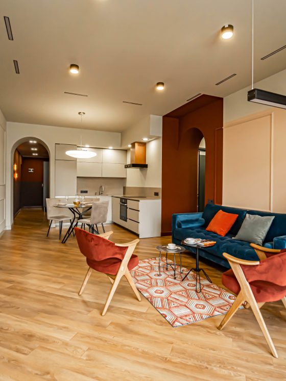 Salon ouvert avec mur terracotta, canapé bleu, chaises rouille, parquet clair, plantes et suspensions