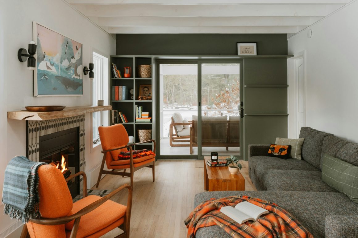 Salon aux nuances vertes et orange aménagé avec cheminée, mobilier en bois et grande baie vitrée