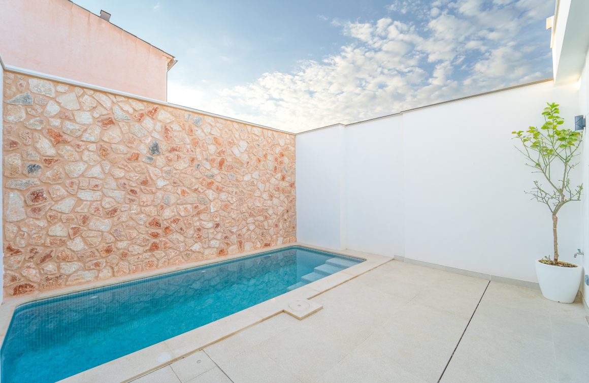 Mur en pierre rosée, sol clair et plante en pot dans une terrasse maison avec piscine