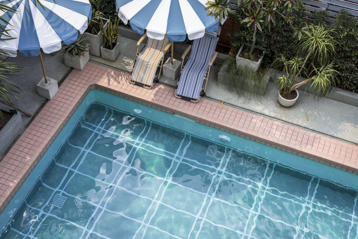 Terrasse avec piscine incluant transats rayés sous parasols, plantes et carrelage pour plage piscine rose
