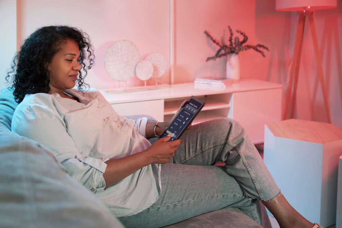 Femme détendue sur le canapé, réglant l'éclairage d'ambiance à l'aide d'une tablette dans son salon