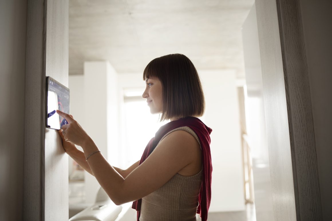 Jeune femme configure sa maison intelligente domotique à l'aide d'un écran mural