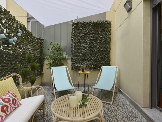 Terrasse aménagée avec fauteuils en rotin, deux chaises bleues, table, plantes et voile d'ombrage
