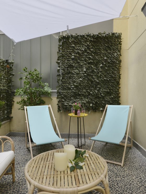 Terrasse aménagée avec fauteuils en rotin, deux chaises bleues, table, plantes et voile d'ombrage