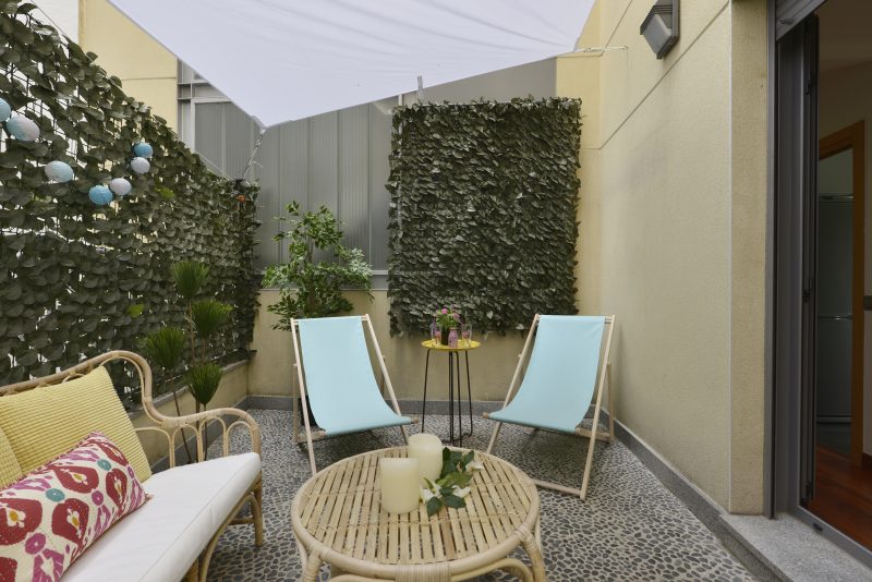 Terrasse aménagée avec fauteuils en rotin, deux chaises bleues, table, plantes et voile d'ombrage