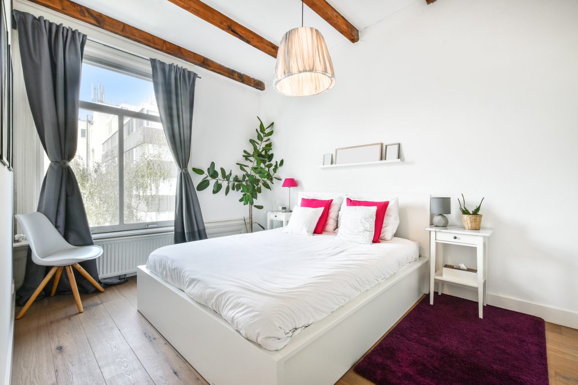 Chambre lumineuse incluant lit large avec matelas épais, couette blanche, coussins fuchsia et parquet