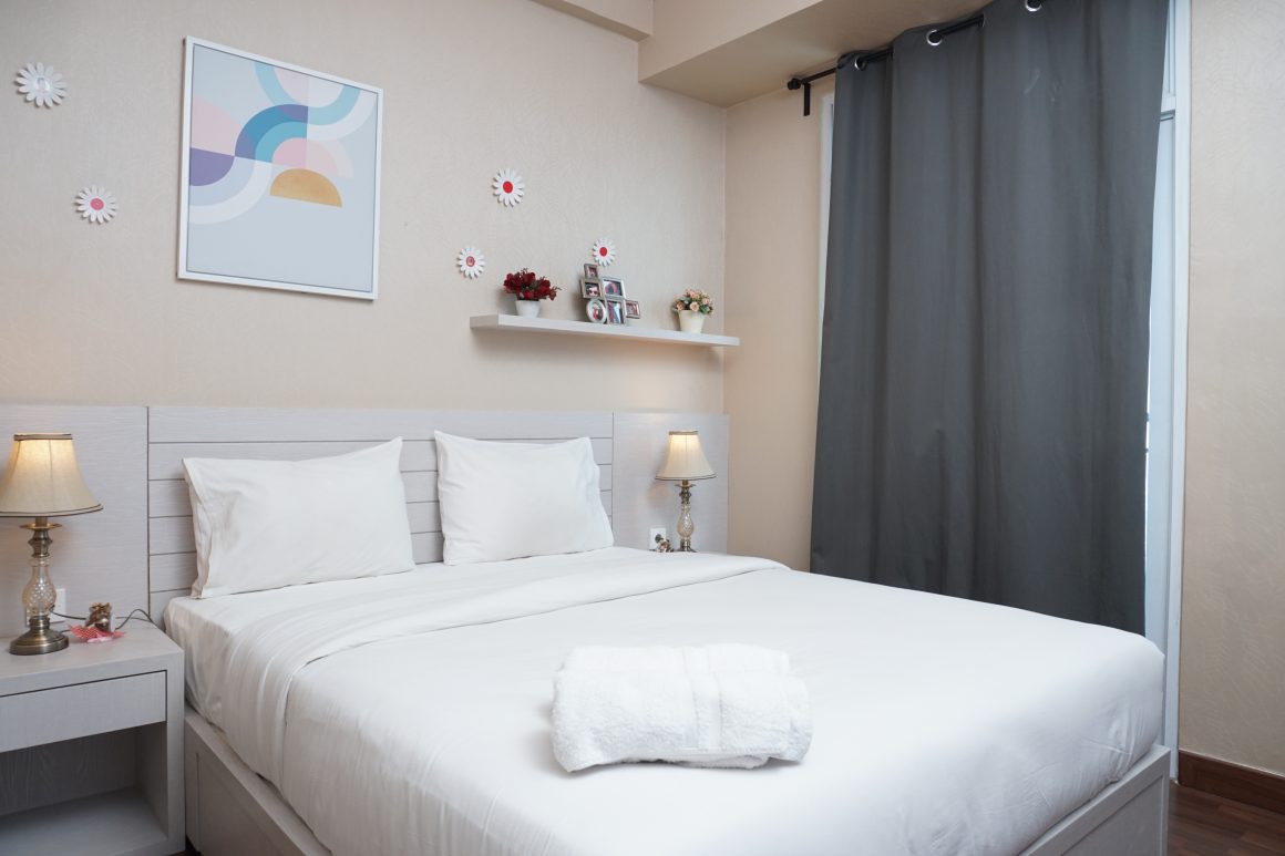 Chambre moderne et épurée : lit double blanc, lampes sur tables de chevet et rideau gris