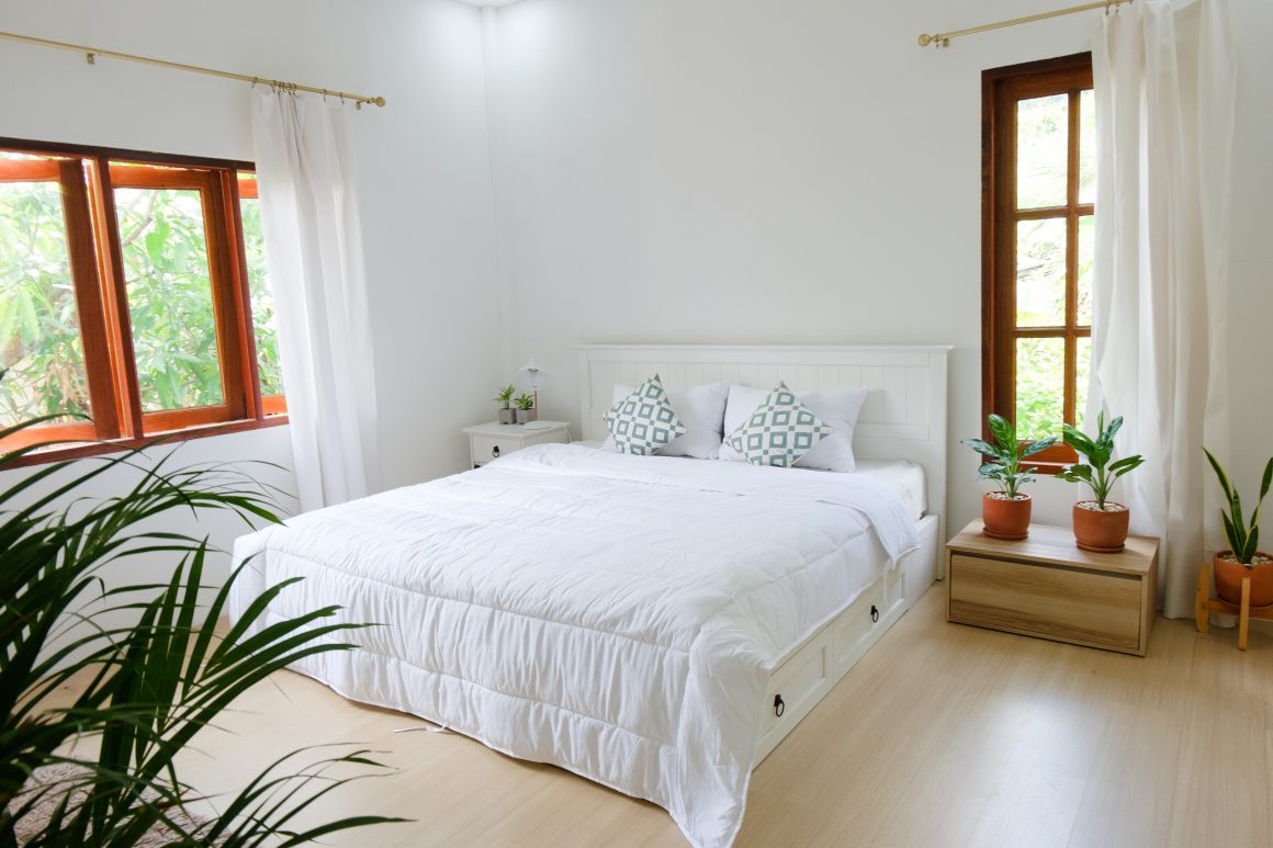 Chambre lumineuse et minimaliste incluant lit blanc, plantes en pot et grandes fenêtres en bois