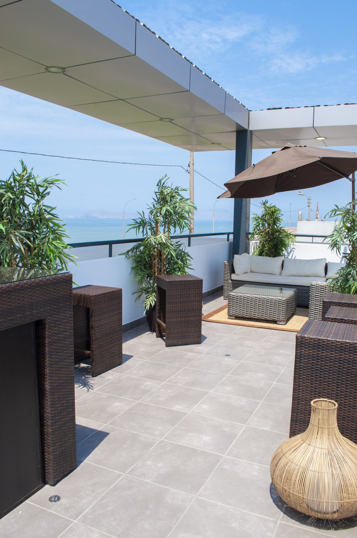 Terrasse moderne : mobilier en rotin, canapé, parasol, plantes et sol carrelé