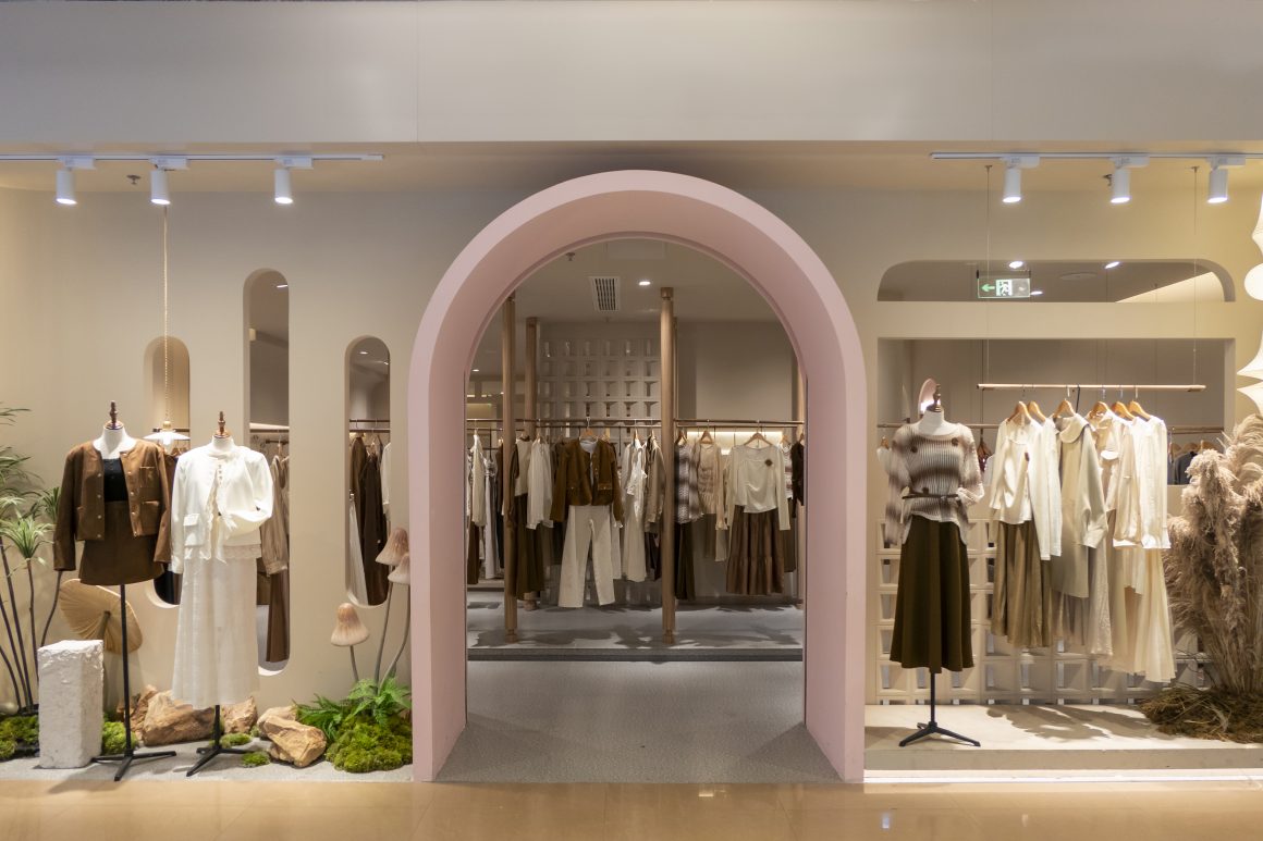 Magasin vêtement femme incluant arche rose, mannequins, présentoirs minimalistes et éclairage doux