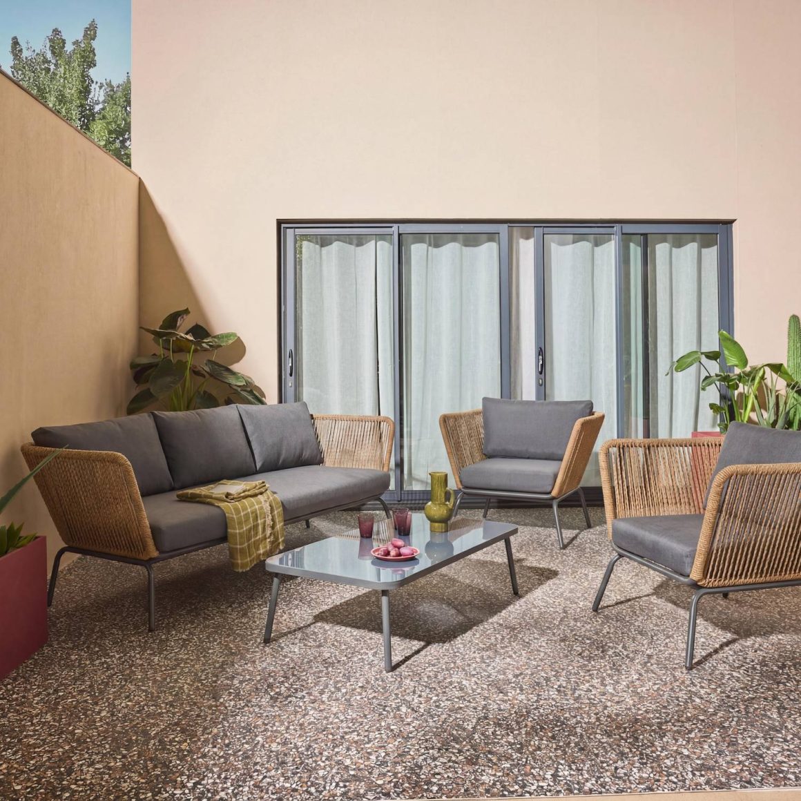Salon de jardin élégant en résine tressée avec coussins gris, table basse et plantes